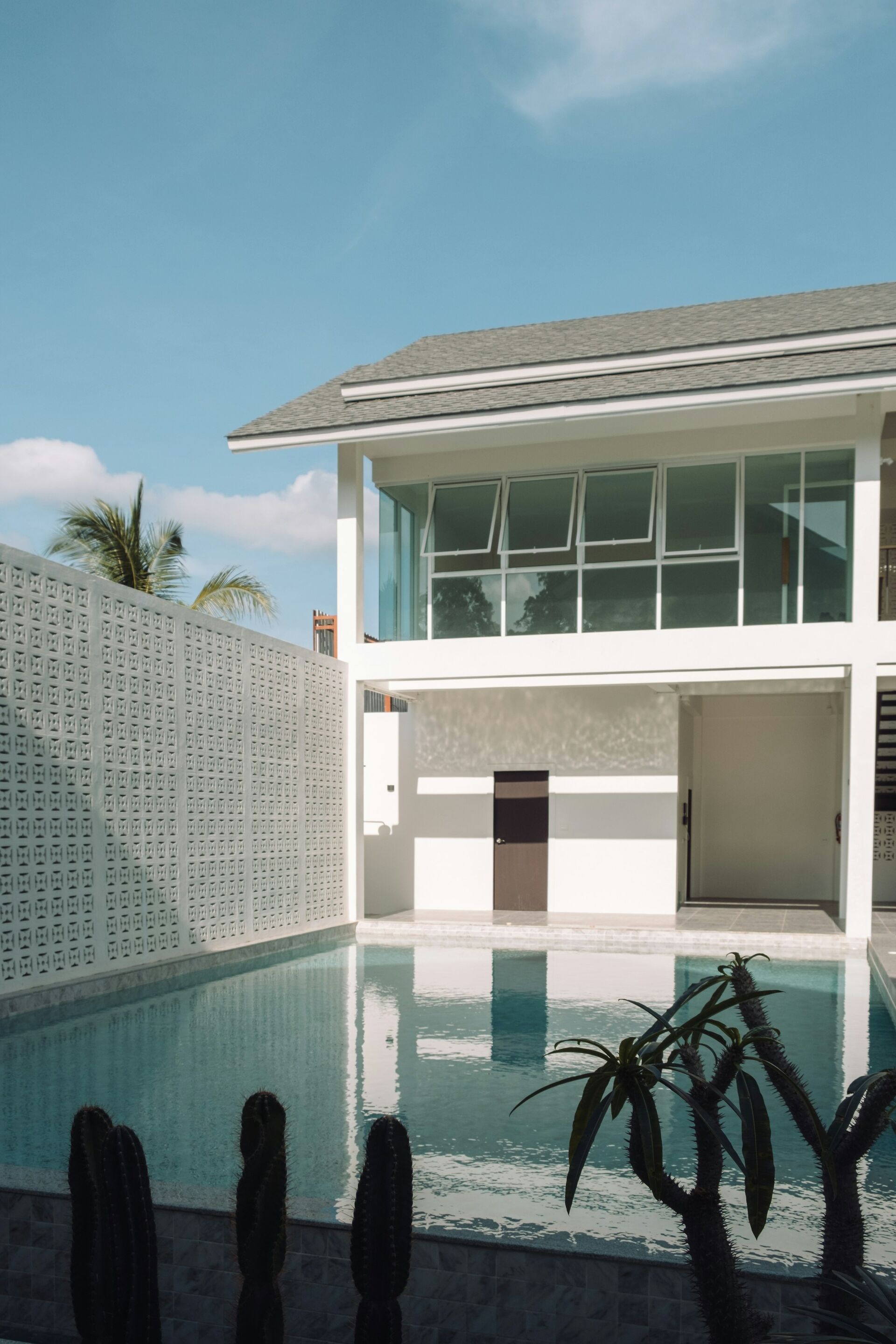 Two-storey white house with a pool and palm trees under a clear sky